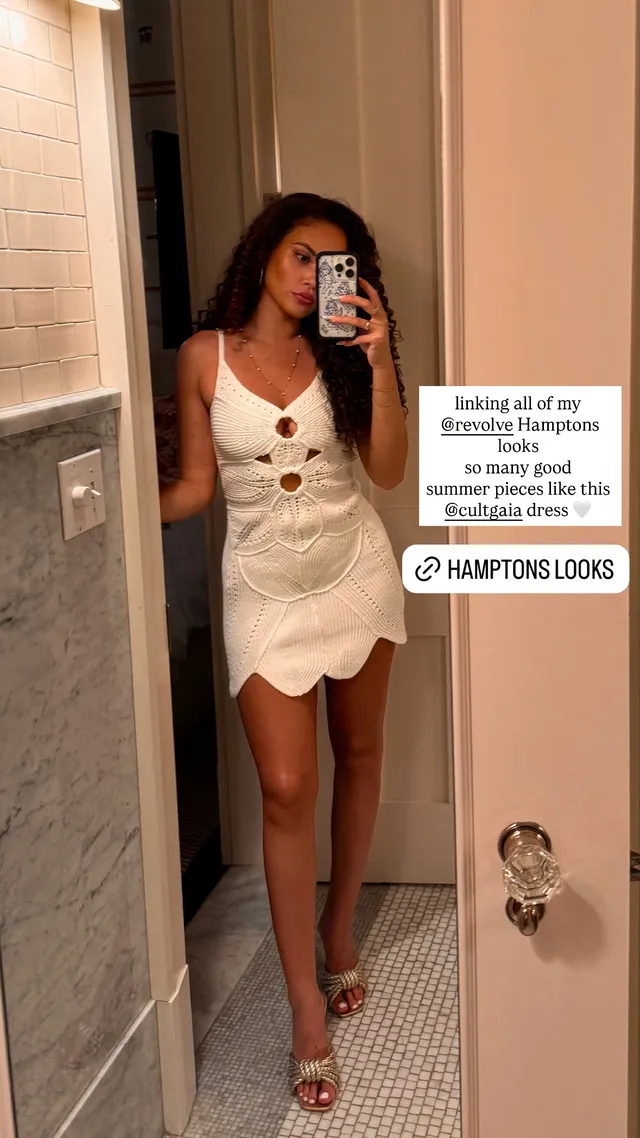 Madison Pettis taking a mirror selfie in a short white dress and pale heels.