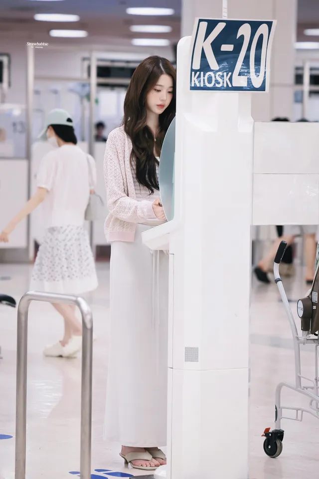 Jang Wonyoung standing at an airport counter in metallic heels.