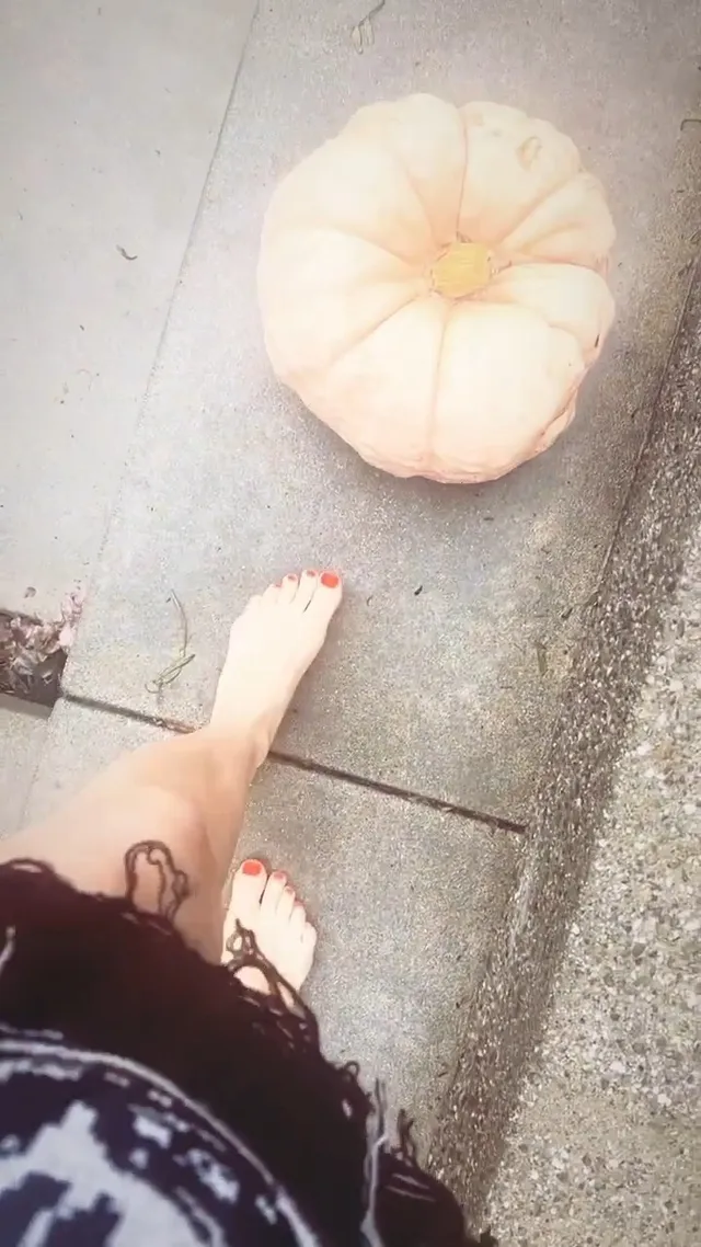 Avril Lavigne standing barefoot beside a pale pumpkin.