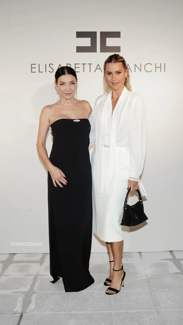 Claire Holt posing beside a companion in a white outfit.