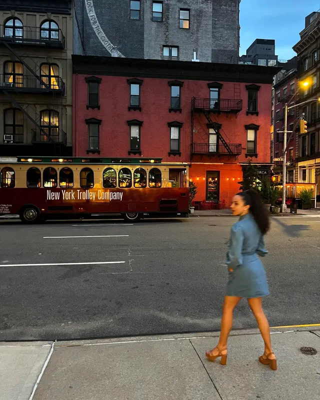 Kiana Madeira walking on a city street in a blue dress and brown heels.
