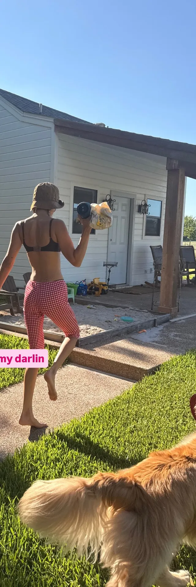 Bella Hadid standing barefoot in a garden.