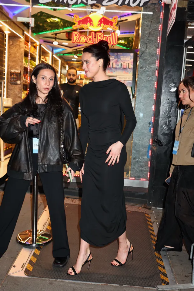 Margaret Qualley standing beside another woman in a black dress and heels.