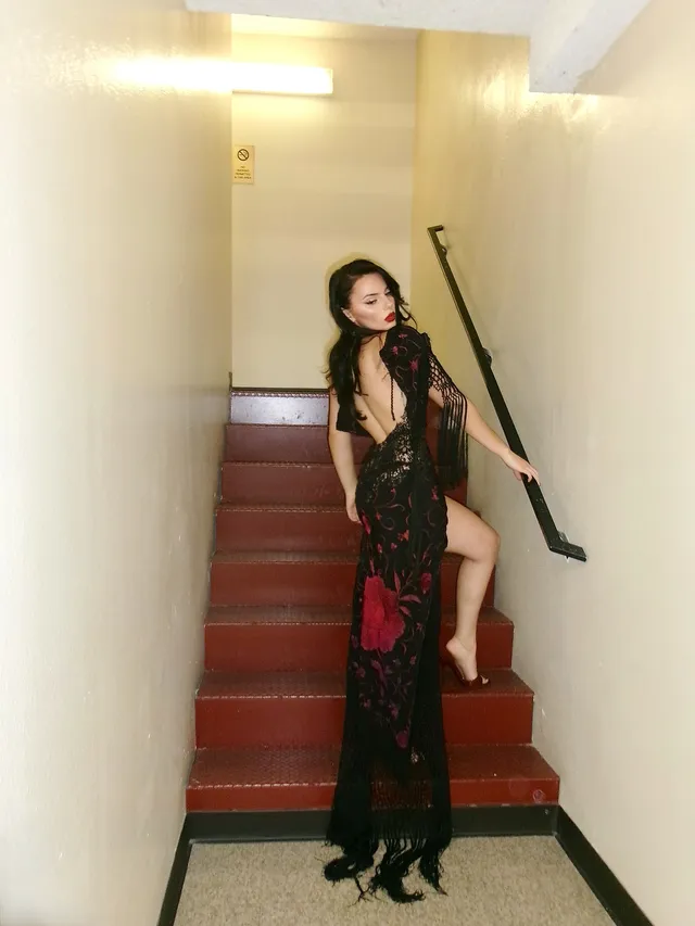 Dafne Keen posing on stairs in a patterned dress and heels.