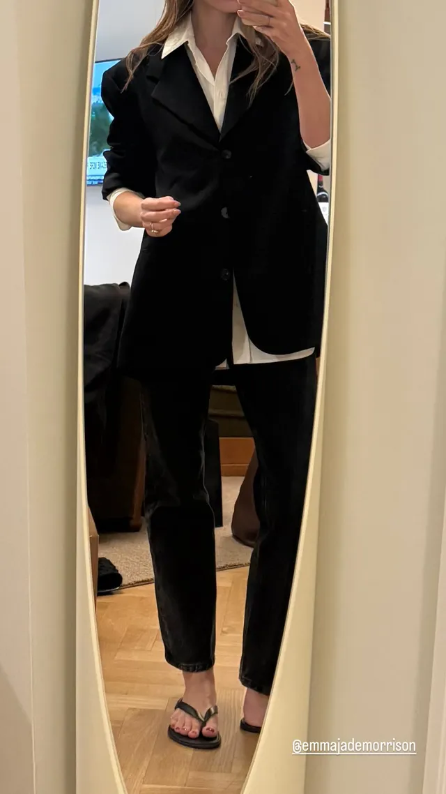 Phoebe Tonkin taking a mirror portrait in a dark outfit and flip-flops.
