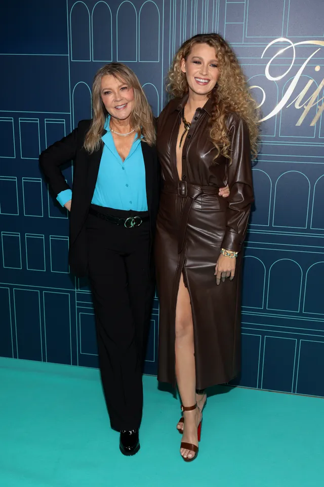 Blake Lively posing with a friend at an event in a dark dress and heels.