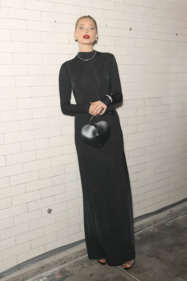Elsa Hosk wearing black heels beneath a long black dress against a tiled wall.