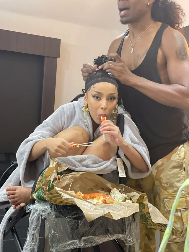 Doja Cat sitting barefoot while having her hair styled.