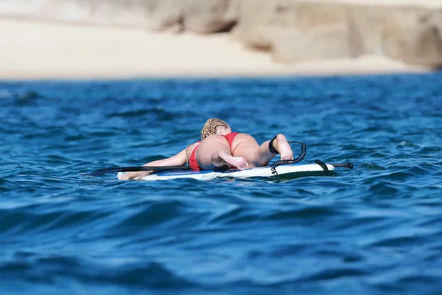 Iggy Azalea lying barefoot on a paddleboard at sea.
