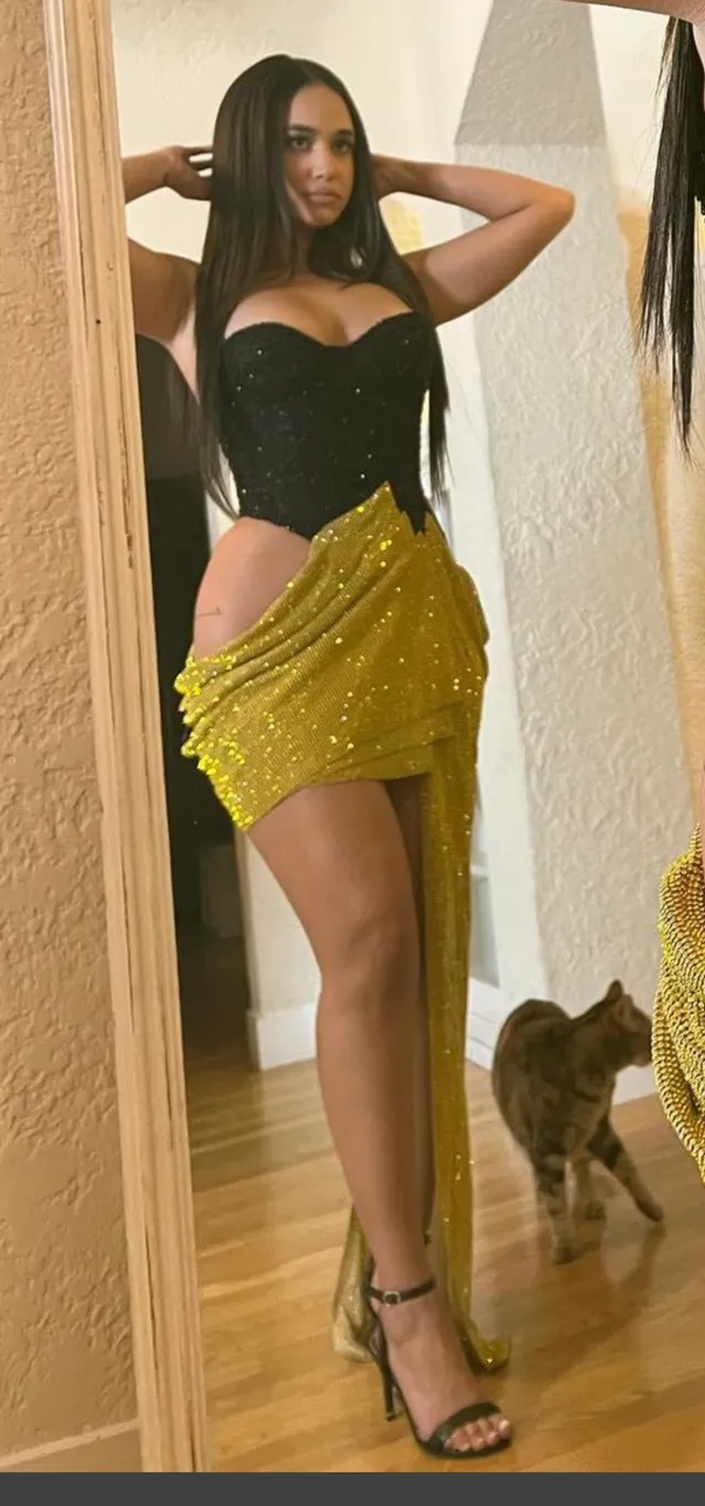 Emily Tosta wearing a yellow skirt and black heels for a mirror photograph.