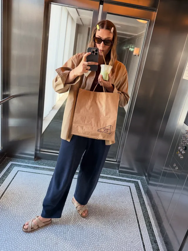 Maria Sharapova taking a mirror photograph in flat sandals and wide-leg trousers.