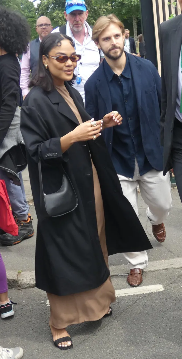 Tessa Thompson walking among guests in a long black coat.