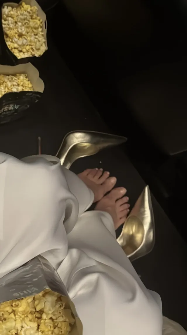 Heidi Klum resting her bare feet beside metallic gold pumps while wearing white.