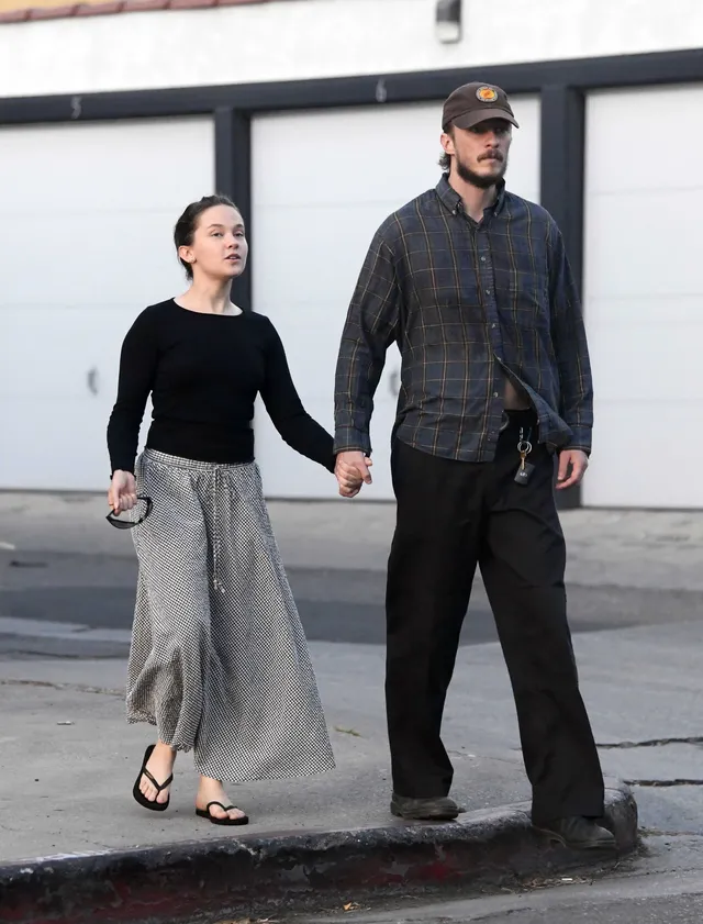 Cailee Spaeny holding hands with a man while walking in flip-flops.