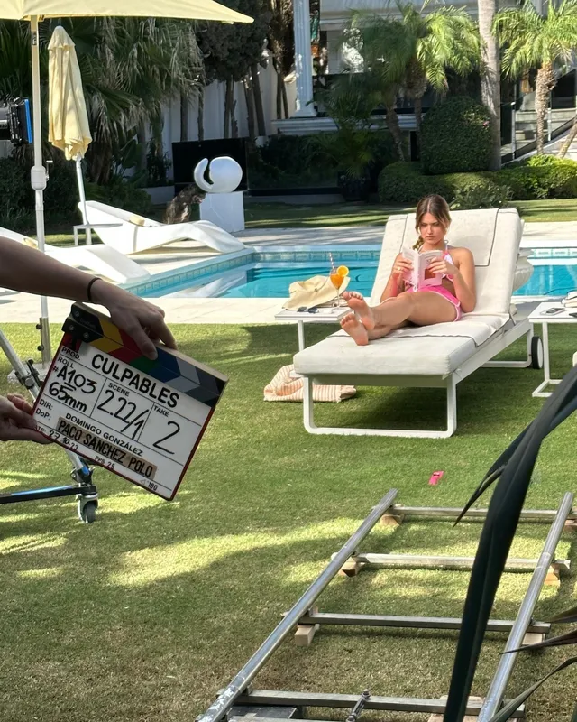 Nicole Wallace reclining barefoot in a pink swimsuit on a pool lounger during filming.