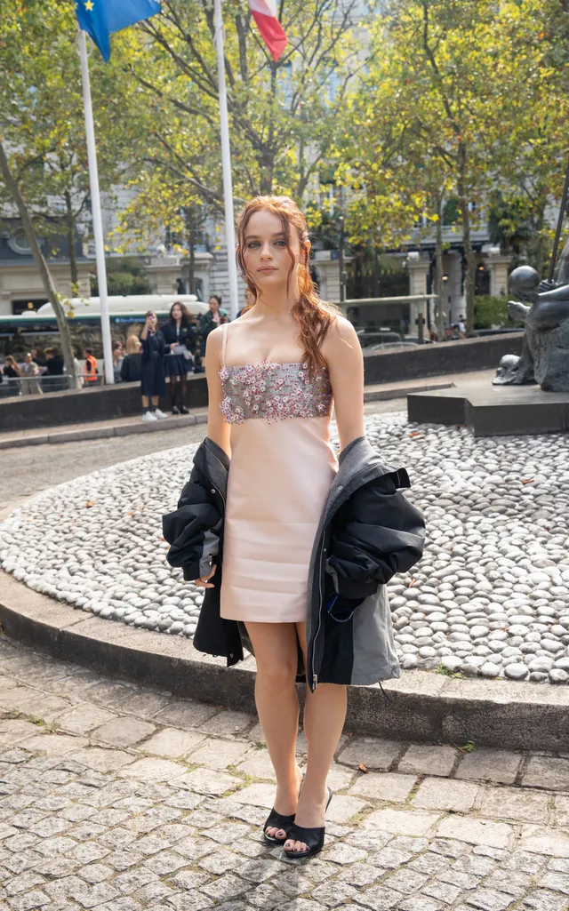Joey King posing outdoors in a pale dress and black heels.