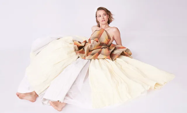 Yvonne Strahovski sitting for a studio portrait in a pale skirt.
