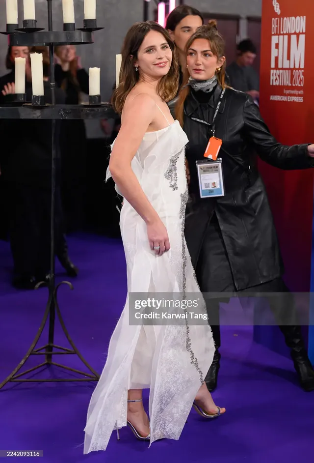 Felicity Jones standing on a premiere carpet in a white gown.
