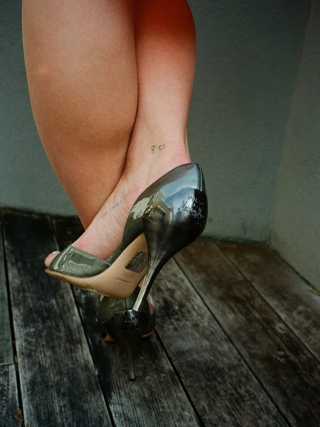 Charli D’Amelio wearing metallic green platform heels on a wooden floor.