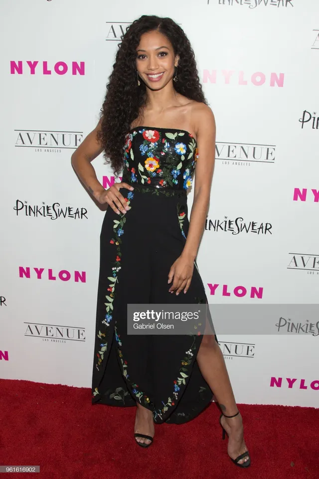 Samantha Logan posing in a floral black dress and heels at an event.