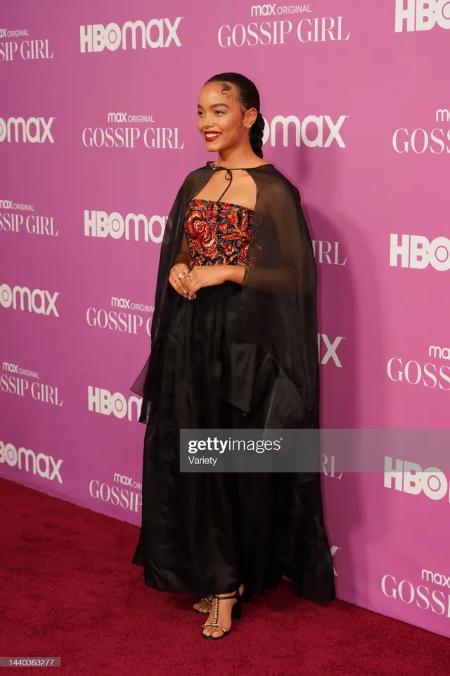 Whitney Peak wearing a dark jacket over an embellished top and gold heels at an event.
