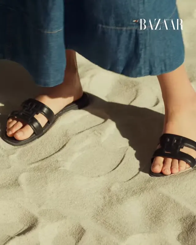 Jisoo wearing black flat slides beneath a blue outfit during a beach fashion shoot.