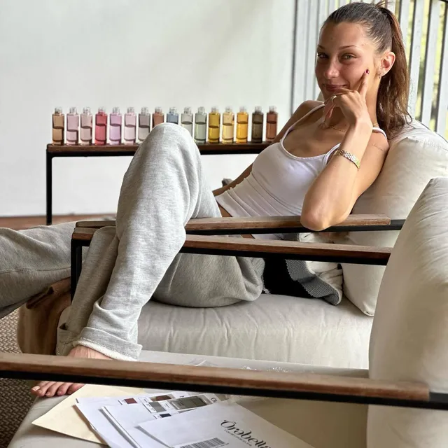 Bella Hadid relaxing in a chair in gray trousers and long pale socks.