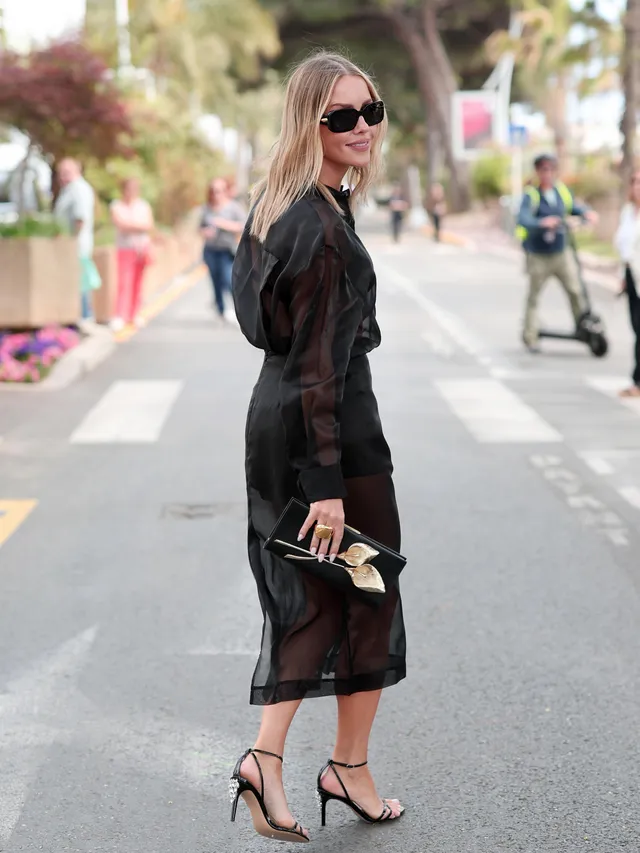 Claire Holt posing on a pavement in a sheer black dress.