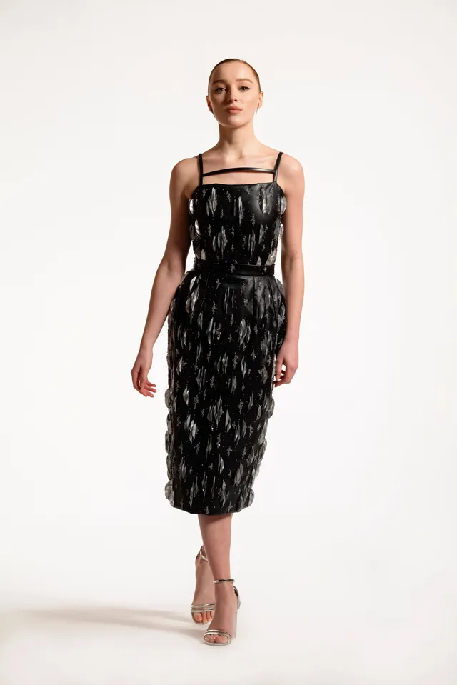 Phoebe Dynevor posing in a black patterned dress against a pale studio background.