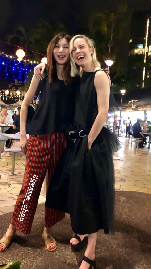 Gemma Chan posing with a friend outdoors at night.