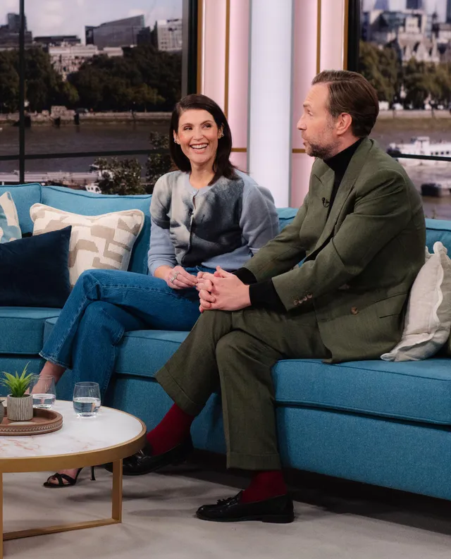 Gemma Arterton sitting on a sofa beside a guest during an interview.