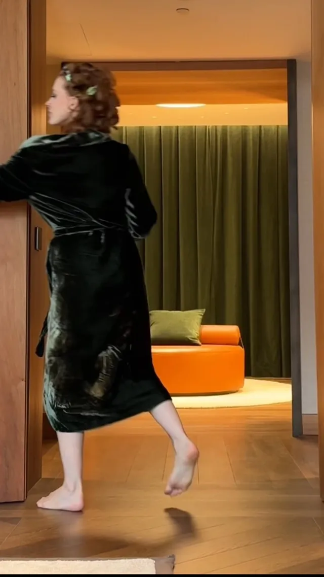 Jessica Chastain walking indoors in a dark robe.