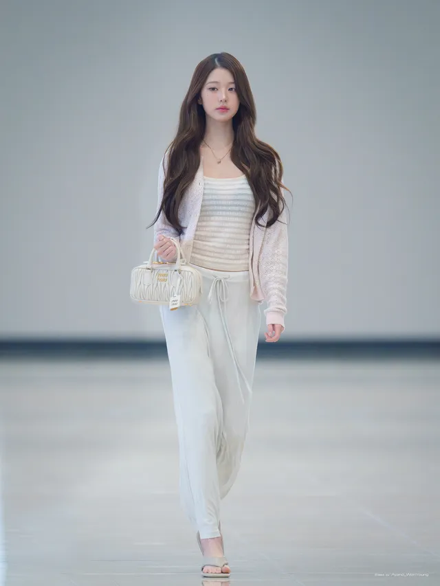 Jang Wonyoung walking indoors in a pale outfit and metallic heels.