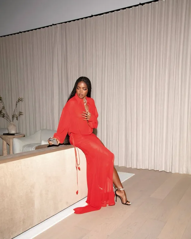 Ryan Destiny posing in a red gown and strappy heels beside a counter.