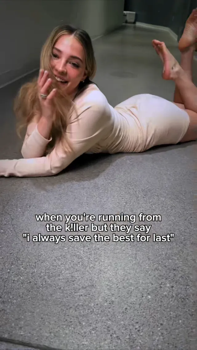 Madelyn Cline lying barefoot on a corridor carpet and waving.