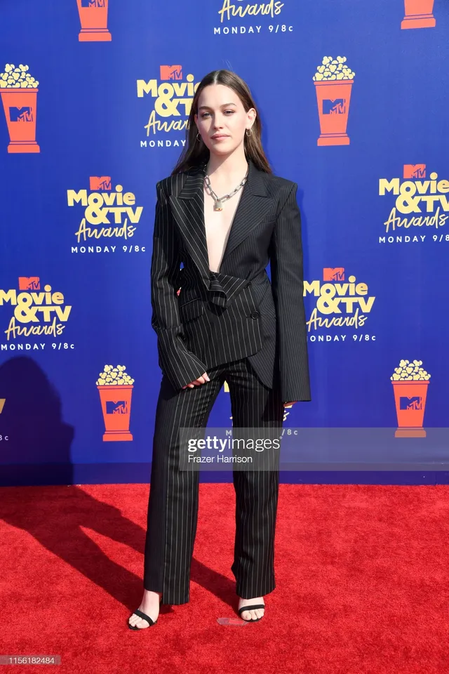 Victoria Pedretti posing against an awards backdrop in a tailored outfit.