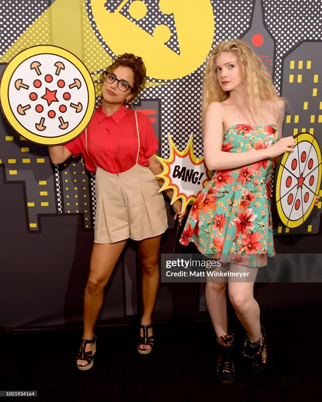 Kiana Madeira posing with a guest in a red blouse, shorts and black heels.