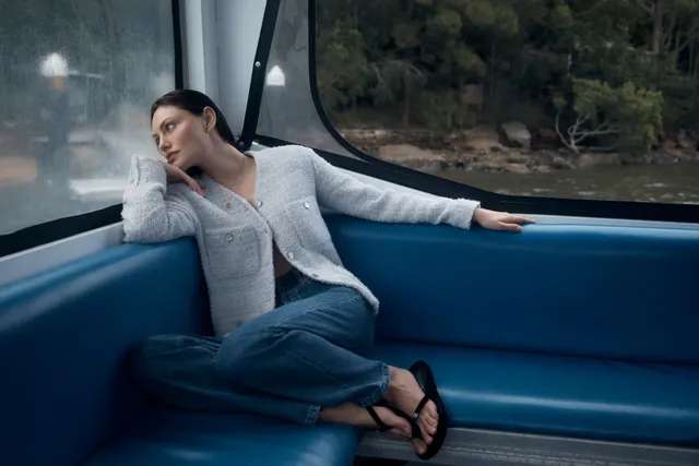 Phoebe Tonkin sitting in a boat in jeans and black flip-flops.