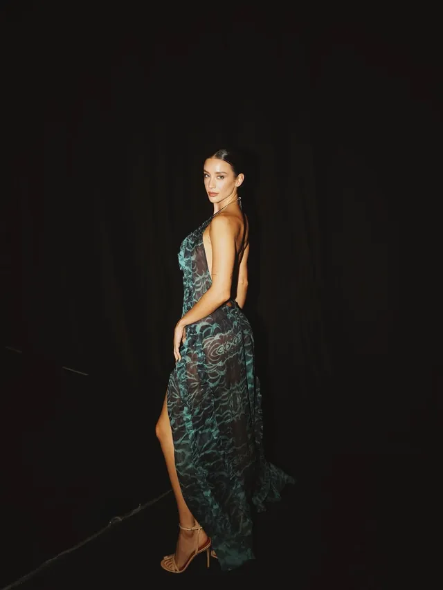 María Pedraza posing in a long patterned green dress and heels at an event.