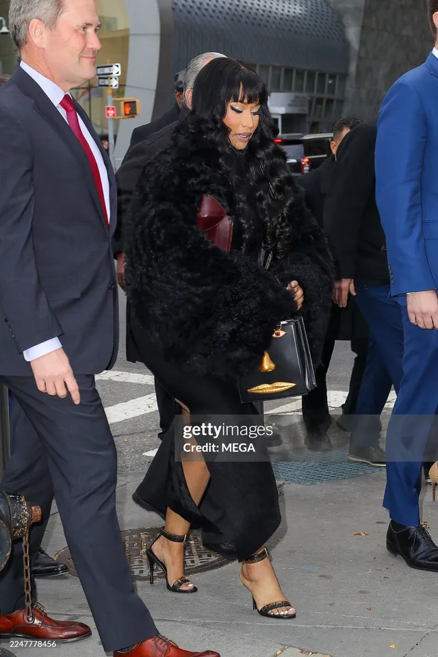 Nicki Minaj walking outdoors in a dark outfit and black heels.