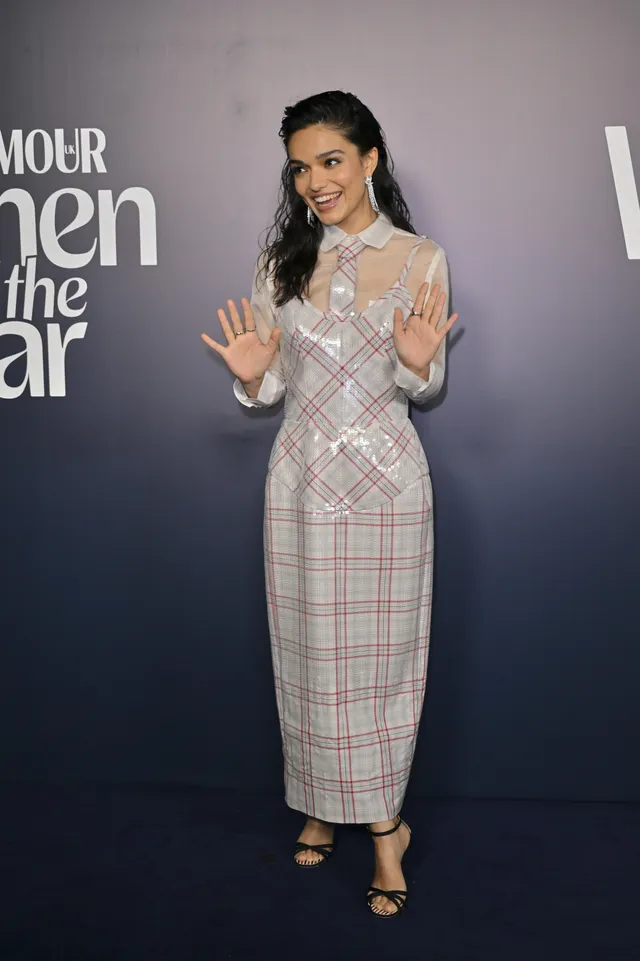 Rachel Zegler waving in a checked dress and black heeled sandals.