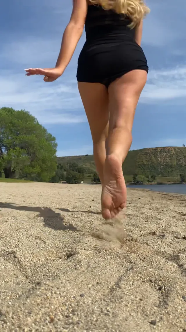 Sabrina Carpenter walking along a sandy lakeshore.