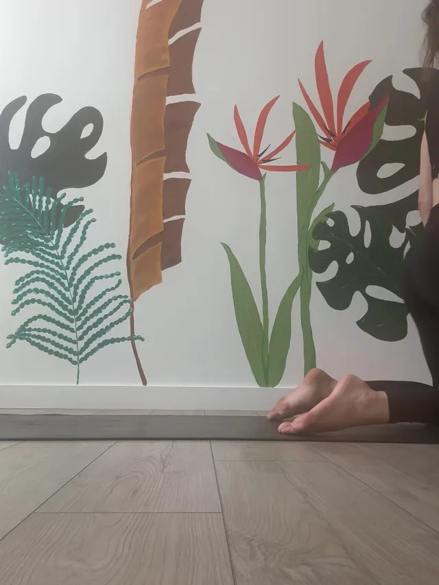 Alexandra Daddario resting a bare foot beside a tropical wall mural.
