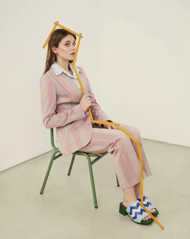 Nicole Wallace sitting on a chair in a pink suit and patterned flat sandals.