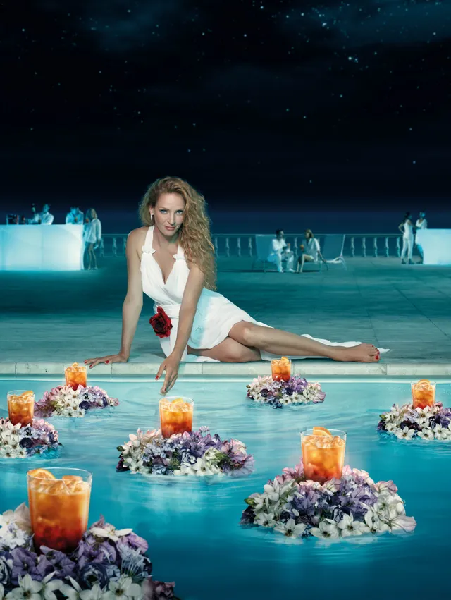 Uma Thurman sitting barefoot beside a pool in a white outfit.