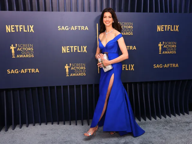 Anne Hathaway posing at an awards event in a blue gown and open-toe heels.