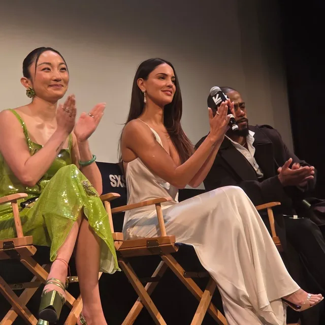 Eiza González sitting in an audience wearing a pale dress and heels.