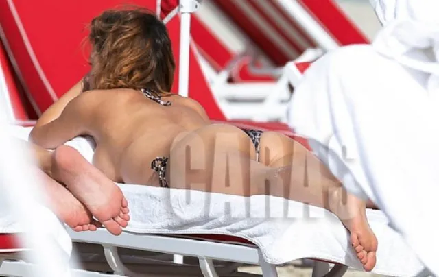 Úrsula Corberó reclining barefoot on a beach lounger in a patterned bikini.