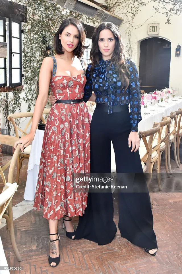Adria Arjona posing beside another woman in a patterned dress and black heels.