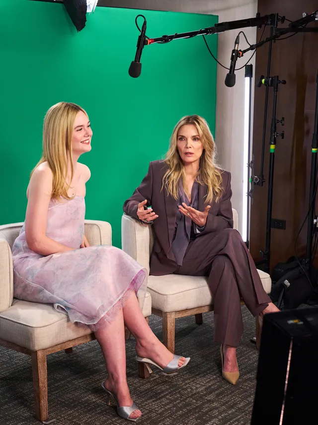 Elle Fanning sitting in a pink dress and silver heels beside another woman during an interview.
